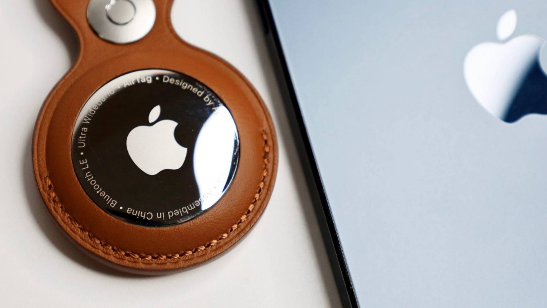 Sledovacie zariadenie Apple AirTag v koženom puzdre vedľa iPhonu