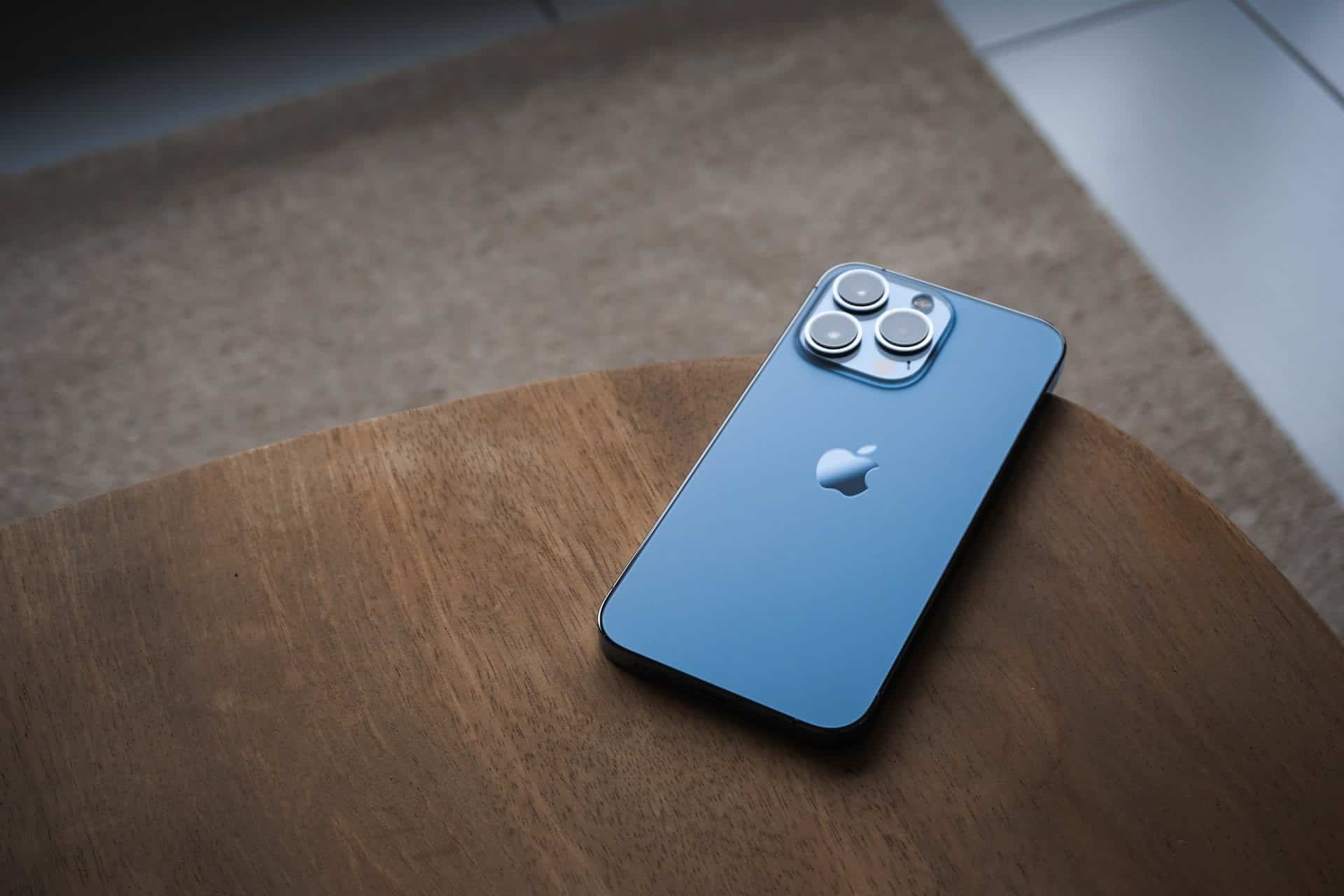 iPhone 13 Pro vo svetlo modrej farbe sierra blue zo zadnej strany položený na drevenom stole
