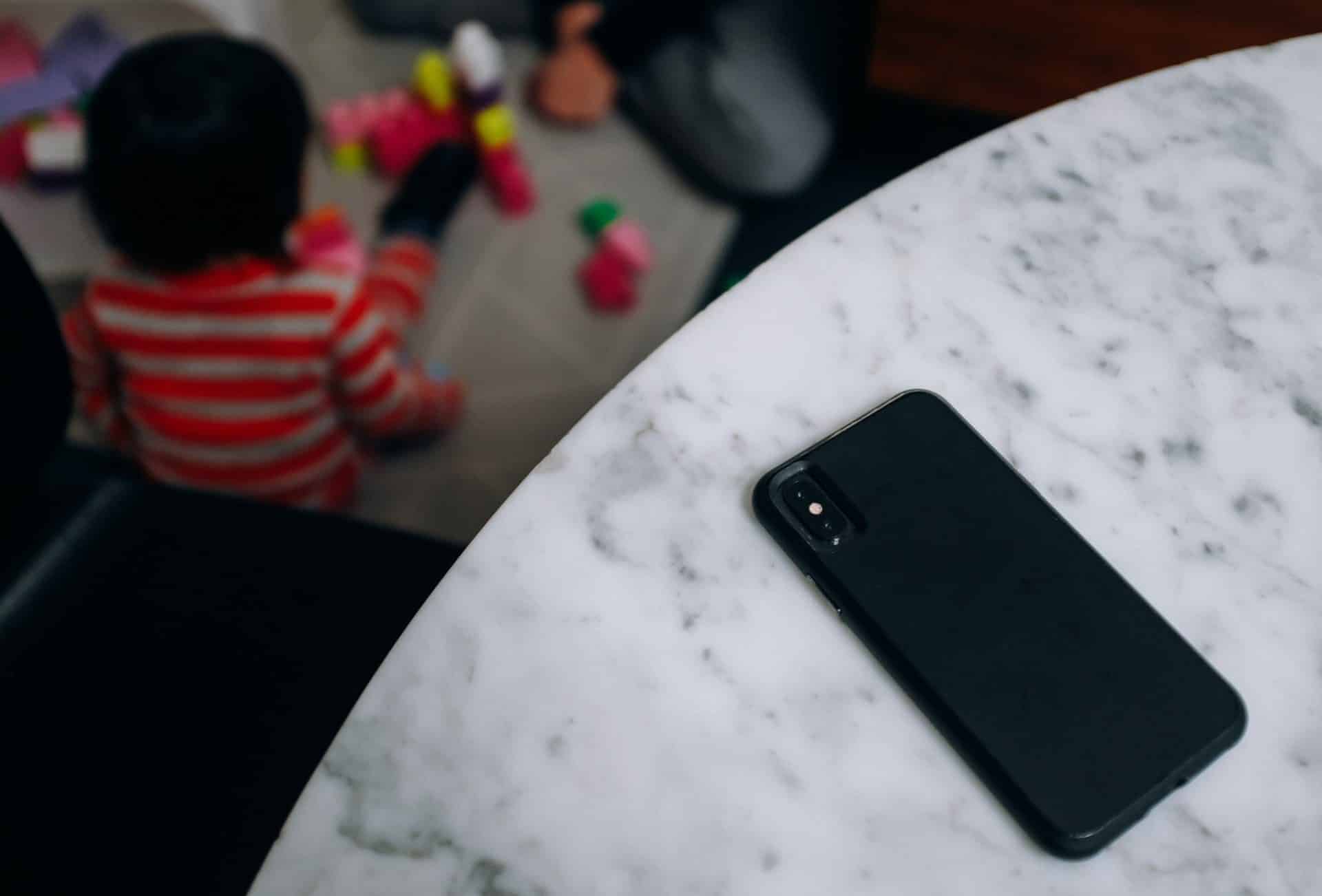 iPhone položený na mramorovom stole a dieťa v pozadí
