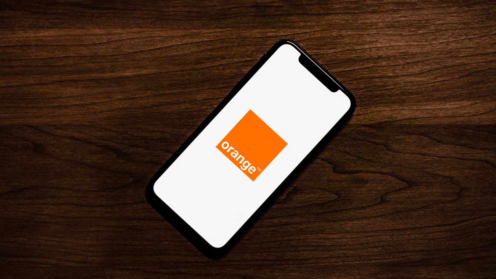 Orange Slovensko na obrazovke iPhonu, ktorý je položený na drevenom stole