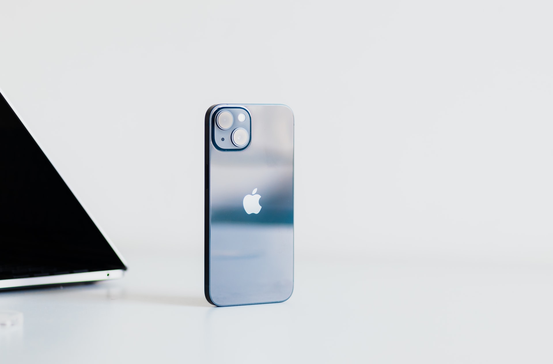 iPhone 13 v tmavomodrej farbe blue s MacBookom v pozadí