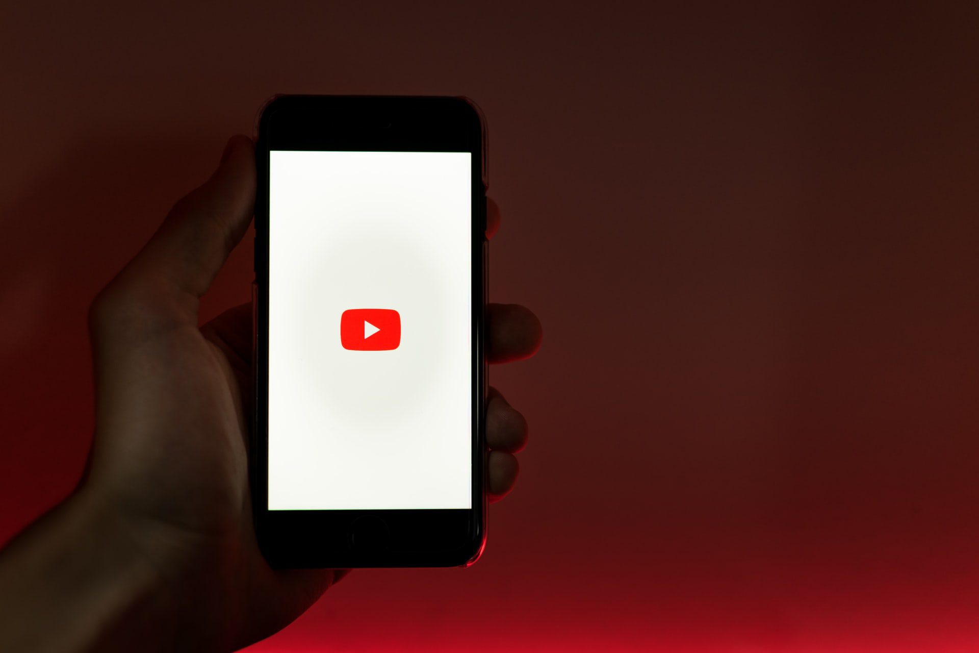 iPhone s aplikáciou YouTube v ruke na červenom pozadí