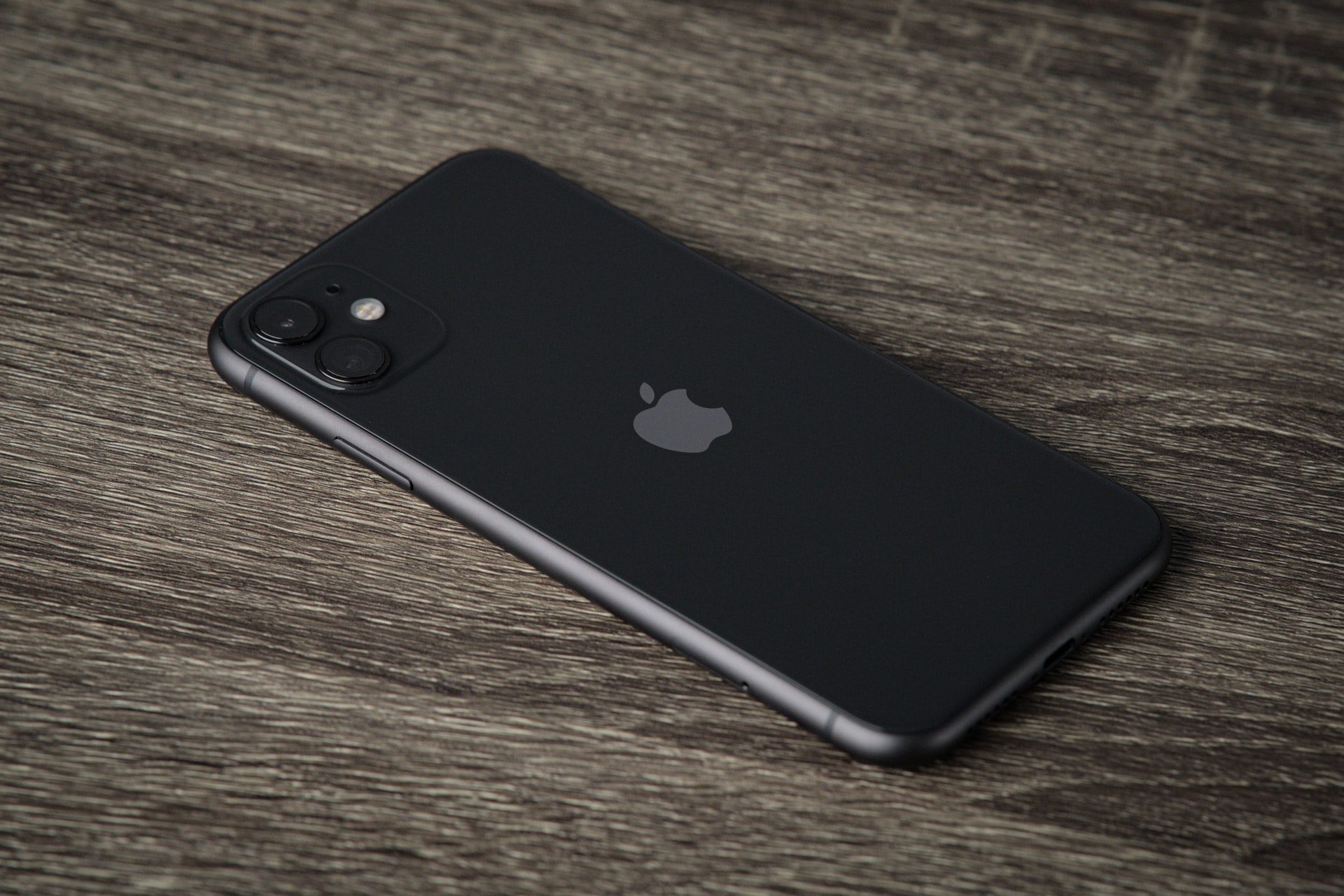iPhone 11 v čiernej farbe položený na drevenom stole. Fotka zo zadnej strany