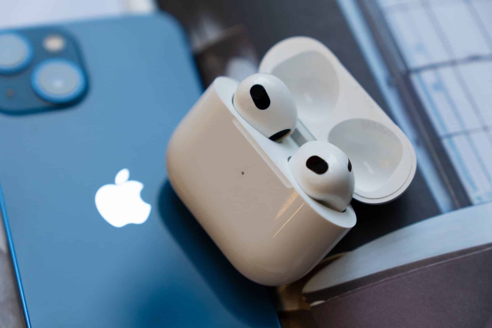 Airpods 3 generácie v nabíjacom púzdre položené na modrom iPhone 13 od spoločnosti Apple