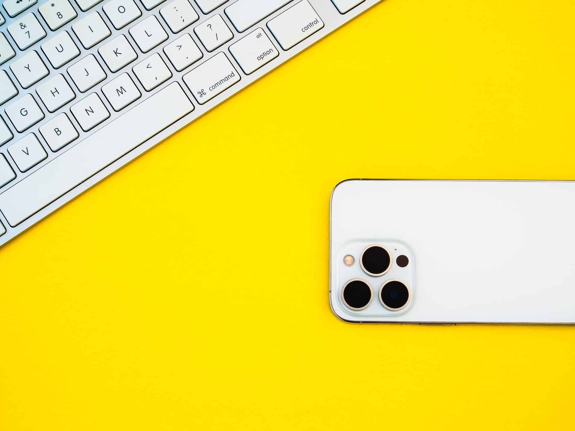 iPhone 13 Pro na žltom pozadí s klávesnicou položenou na stole