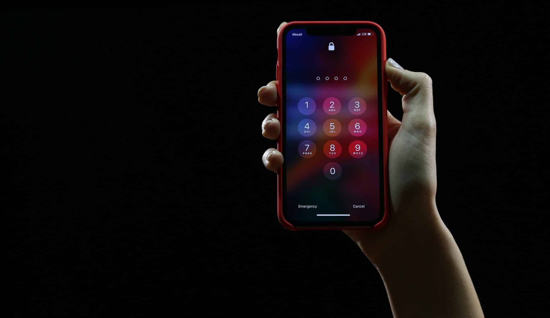 Červený iPhone 11 v ruke v tme. Na displeji svieti heslo, respektíve žiadosť o číselný kód